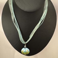 Abstract circular glass floral design pendant on baby blue cord/ribbon necklace