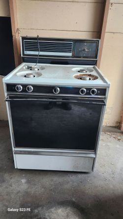 Vintage White-Westinghouse gas range is white with black and chrome accents. It has four burners and a central oven with a large glass door. Control p