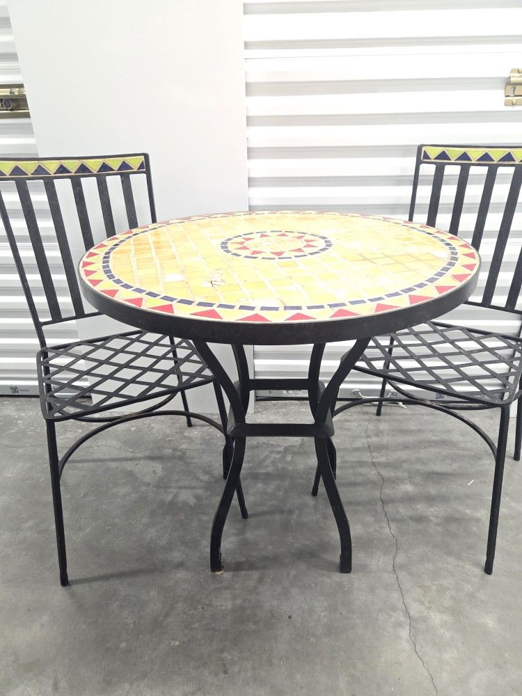 Small round mosaic tile bistro table with wrought iron frame and two matching wrought iron chairs.