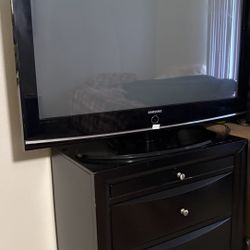 Samsung flat panel TV, with sturdy black 3-drawer TV stand.