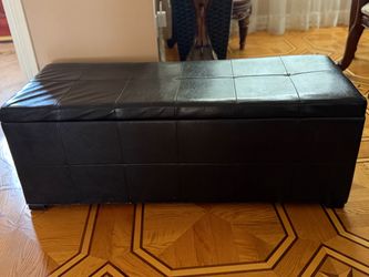 The ottoman is a long, rectangular black faux-leather storage ottoman