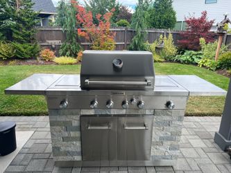This is a KitchenAid Stainless Steel Outdoor Grill Island featuring faux stone veneer siding and a built-in gas grill head.