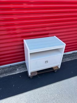 modern white nightstand/bedside table featuring an integrated frosted glass top, an open storage cubby, and a single lower drawer with a central squar