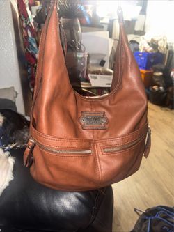 This preowned Nicole Miller brown leather hobo bag features distinctive front zipper pockets and decorative stitching around the brand plaque. Used bu