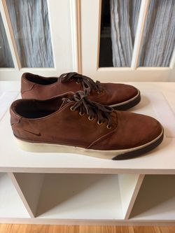 These are Nike SB Zoom Stefan Janoski skate shoes in a Brown Leather / Ale Brown colorway featuring brass metal eyelets and debossed Nike Swoosh logos