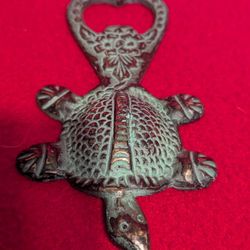 A cast iron turtle-shaped bottle opener with a verdigris patina