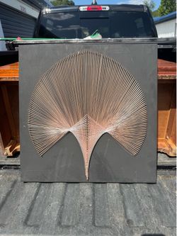 geometric string art piece features intricate thread patterns stretched between nails arranged on a dark board.