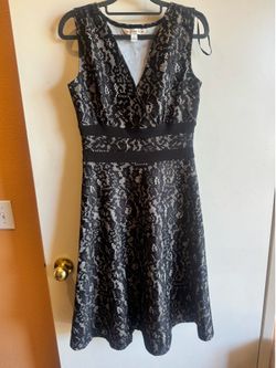 Sleeveless A-line dress with floral black lace overlay with sequins look. Waistband detail defines the silhouette. Elegant and versatile for any event
