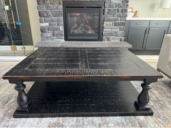 Rustic farmhouse-style square coffee table with a distressed black finish and turned pedestal legs