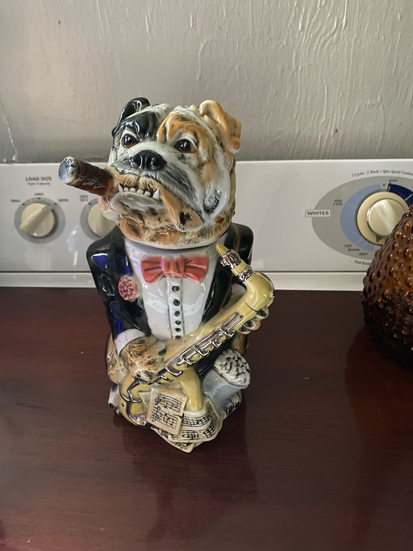 a collectible bulldog figurine, specifically a beer stein, featuring a bulldog dressed in a tuxedo and holding a saxophone while smoking a cigar