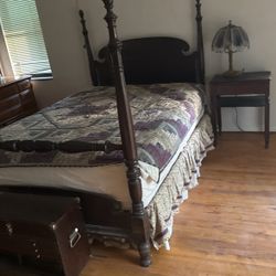 An antique bed with a night stand, drawer, ottoman  and a chair