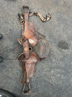 Vintage tooled leather Western saddle with decorative floral tooling, stirrups, straps, and matching tack.