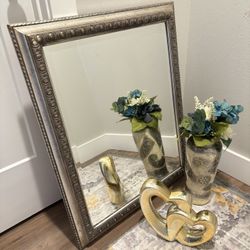 Elegant decorative set including a vintage-style framed mirror, a detailed ceramic vase with artificial flowers, and a gold intertwined heart ornament