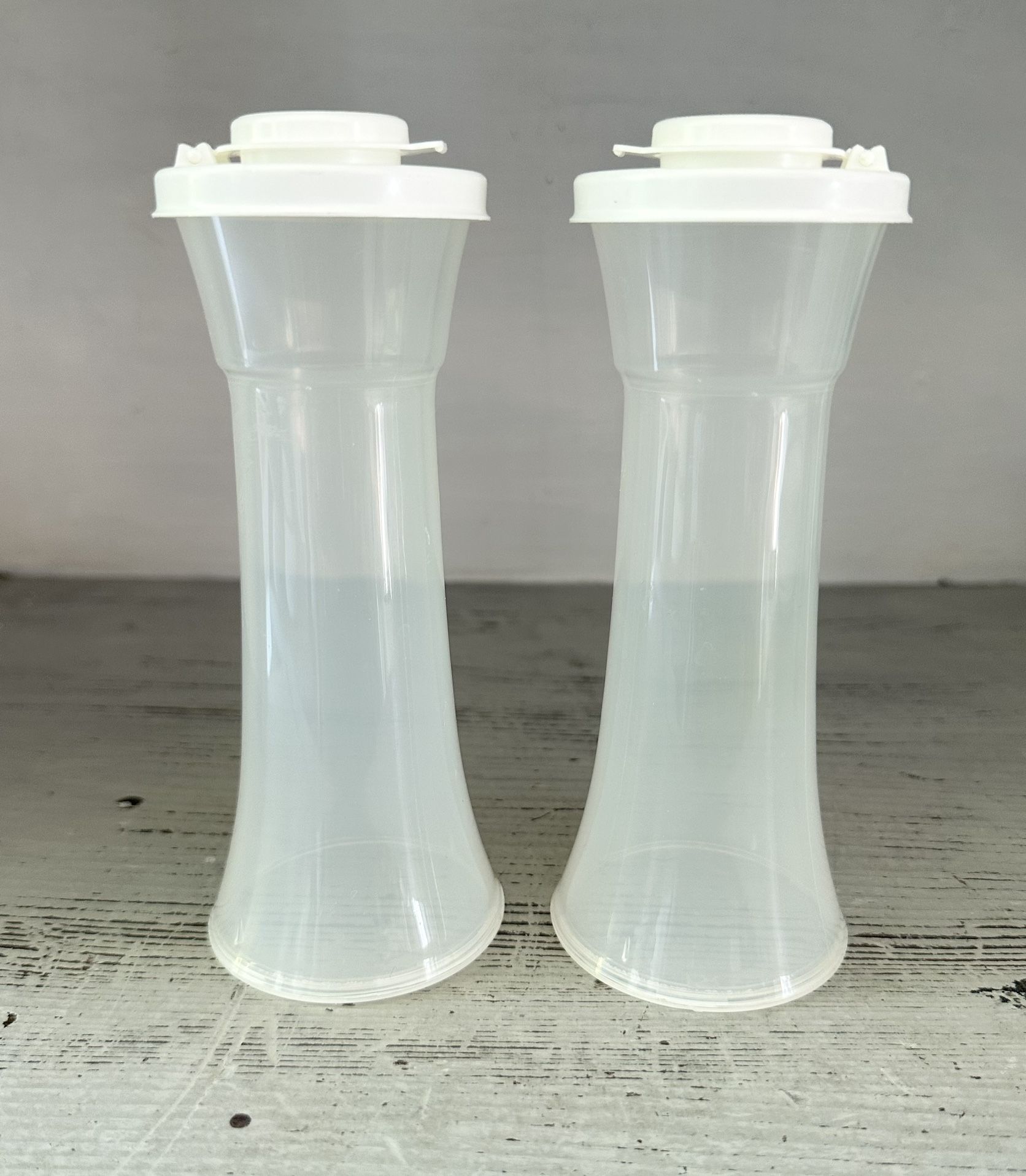  Tupperware hourglass salt and pepper shakers. Unused.  Clear body with white lids. These are the large size at 6 1/4” tall. 