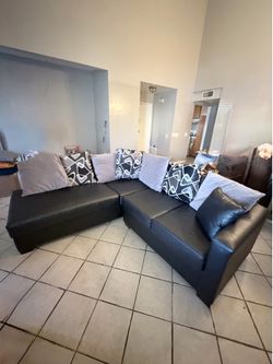 black faux leather sectional features a contemporary L-shaped design and comes with several decorative throw pillows.