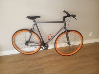 a Retrospec Harper Single-Speed Fixed Gear Urban Commuter Bike in the Matte Graphite & Orange colorway.