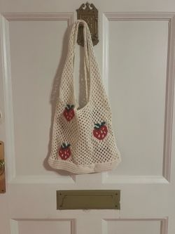 Cute cream mesh tote bag. Bag has knitted design with three red strawberries. Handles are part of bag structure.