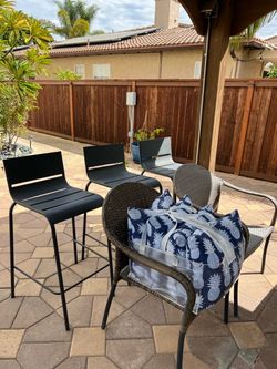 Outdoor metal barstools, two outdoor wicker chairs, and a set of outdoor pillows