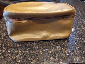 Estée Lauder gold travel cosmetic case. It is a metallic faux-leather makeup pouch featuring a zipper closure complete with a circular charm zipper pu