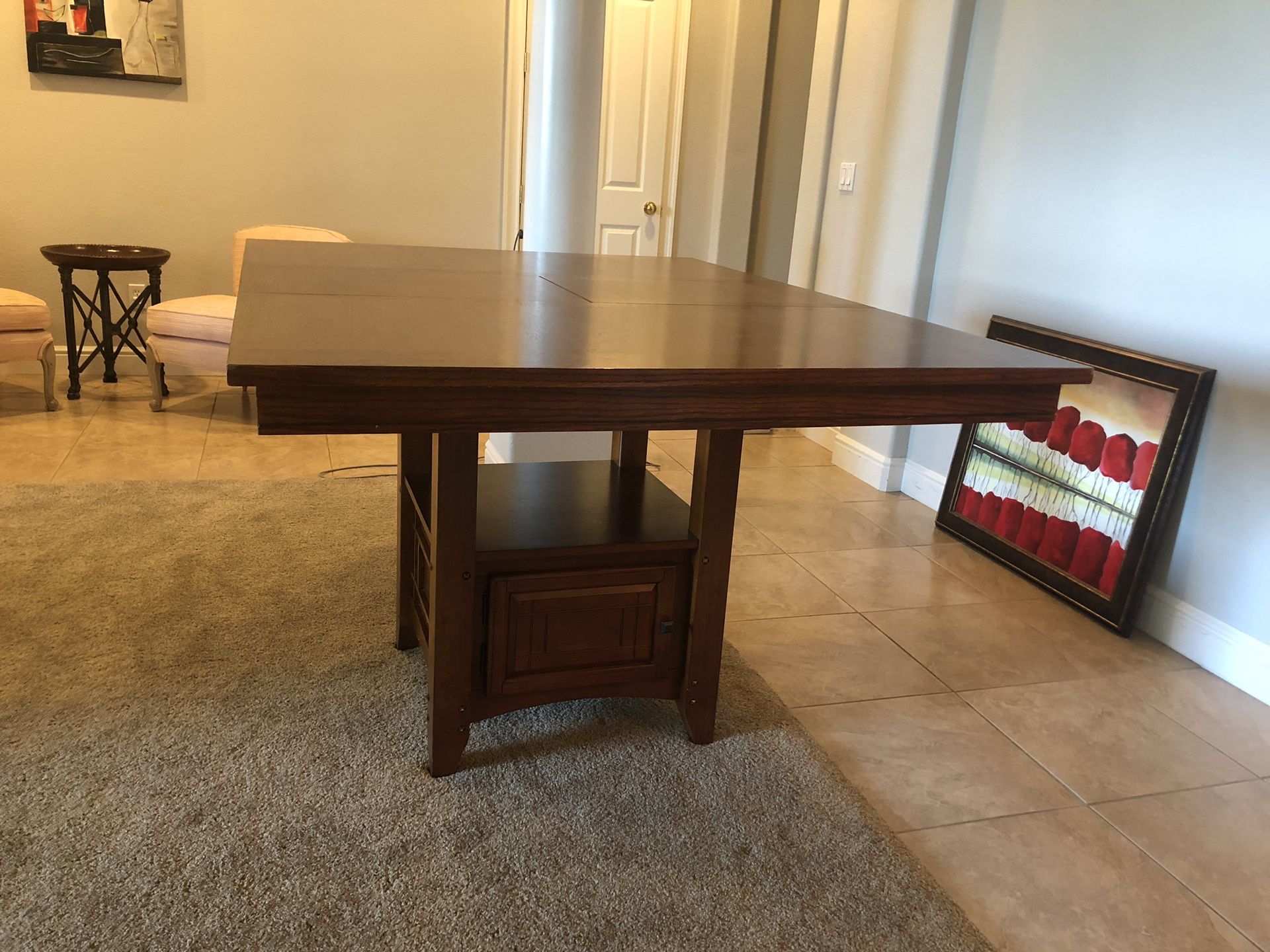 Bar height wood dining table. Can be square 48”x48” or rectangle with a middle leaflet. It has a storage and shelf under and is used but as good as n