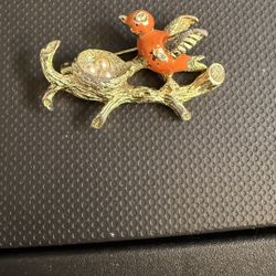 a vintage enamel bird brooch featuring an orange bird on a branch with a nest containing faux pearl egg