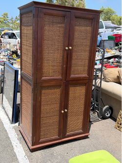 Pier 1 Imports brown armoire or cabinet, which features a solid wood frame with distinctive rattan or wicker woven panels on the do