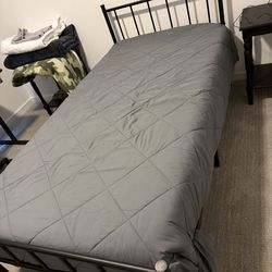 Twin metal bed frame with mattress and bedding.