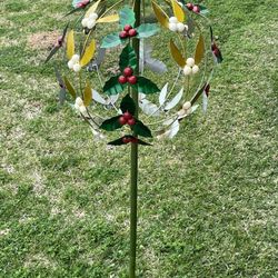 A decorative metal garden wind spinner with a holly motif. Stand 42” Tall When Fully Into The Ground.