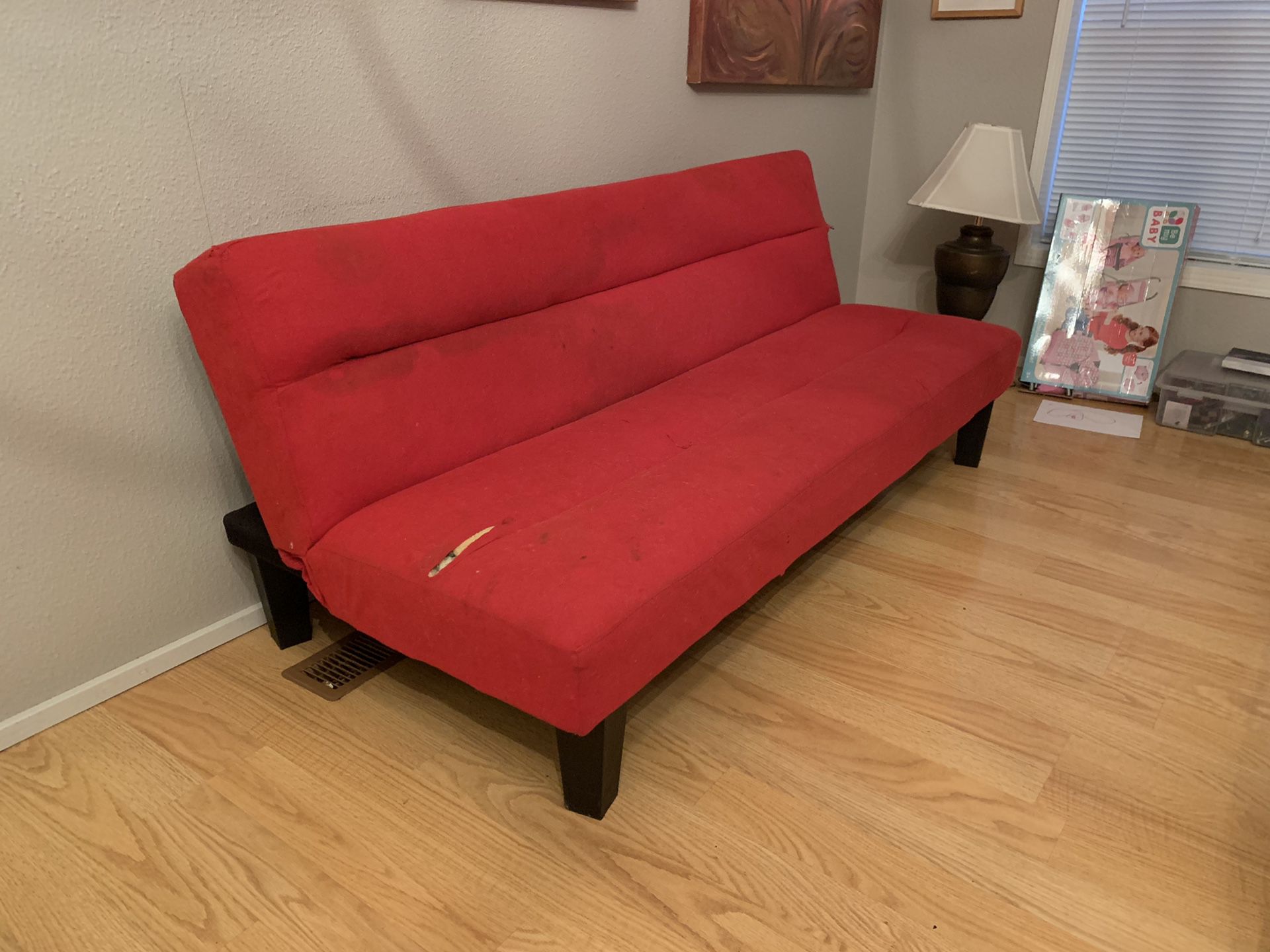 Red small kids futon couch has a couple rips in it
