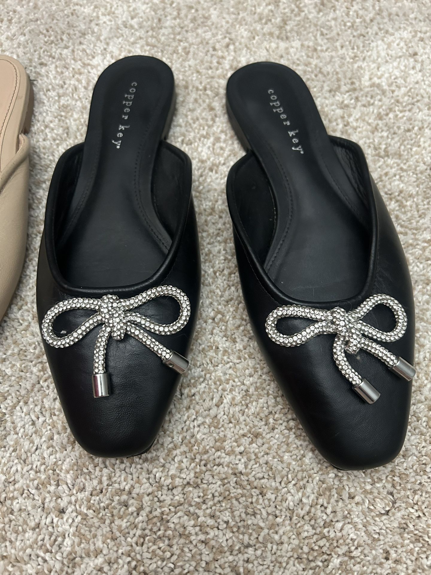 This is a pair of Copper Key black slip-on mules with a rhinestone bow