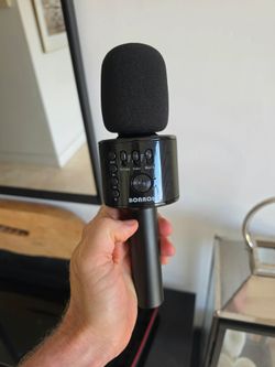 Wireless Bluetooth Karaoke Microphone in its black zippered protective case, featuring a black metallic finish, foam pop filter, and contr