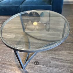Modern round glass accent table with a dark metal tripod base.