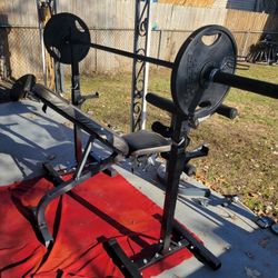 CAPS. 7' OLYMPIC BAR WITH CLIPS.   2-45LB GOLD'S GYM  OLYMPIC PLATES   ADJUSTABLE BENCH WITH LEG EXTENSION WITH ATTACHED CURL BAR. PREACHER  PAD.  POR