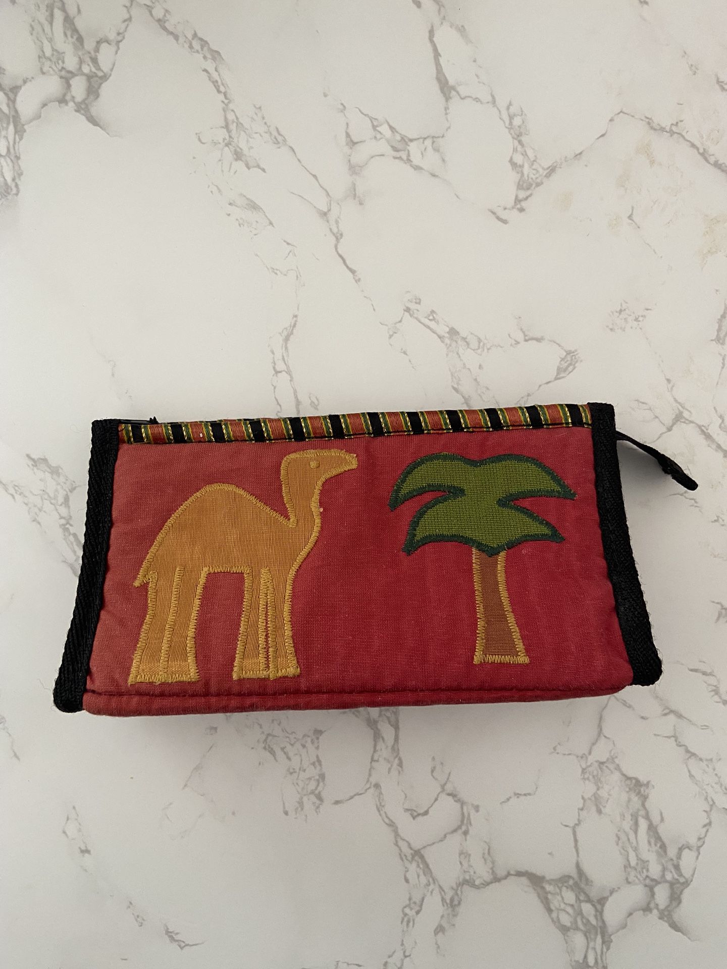 Red fabric pouch with camel and palm tree embroidery.