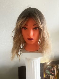 Synthetic hair wig has a dark brown to ash blonde ombre color transition. The hair is styled with loose waves and face-framing curtain bangs. It has a