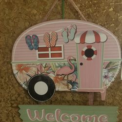 Colorful camper-shaped welcome sign with flip-flops and flamingo design.