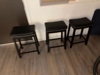 black backless saddle-style counter stools featuring faux leather padded seats and silver nailhead trim.