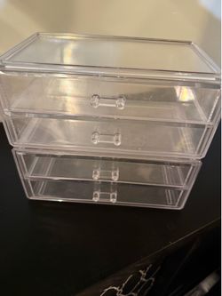 Transparent acrylic storage unit has four drawers with small pull handles. This clear plastic organizer is designed for makeup, jewelry, or office sup