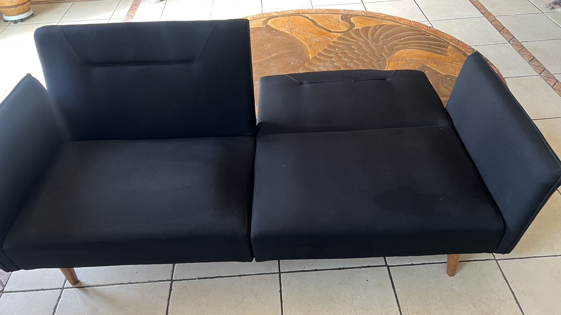 A modern sofa bed / futon with soft black fabric and peg legs