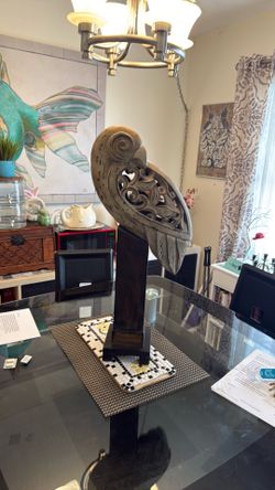 A hand-carved wooden parrot sculpture on a dark wood pedestal.