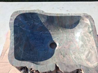 Unique vessel sink is carved from natural stone with a petrified wood aesthetic. Polished interior has green, grey, and pink veining. Exterior has a r