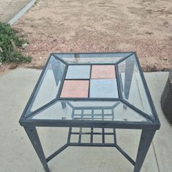 square outdoor patio table with a metal frame and a glass and tile top. 