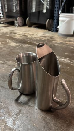 Set of 12 stainless steel milk frothing pitchers used in a commercial setting.