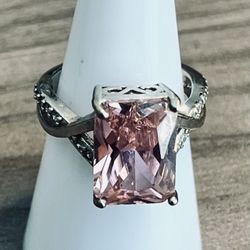 Elegant pink cushion-cut center stone set in a silver-tone band. Features delicate side accents for added sparkle. Stylish pink ring suitable for ever