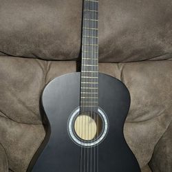 Sleek matte black acoustic guitar has nylon strings and classical style headstock. Body is wood with a smooth dark finish. Great for practice or learn