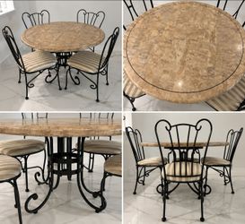 round stone-top dining table with a black wrought-iron base, paired with four matching metal-framed chairs featuring striped upholstered cushions.