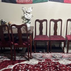 traditional dining set consisting of a dark wood table and matching 6 chairs with red patterned upholstery.