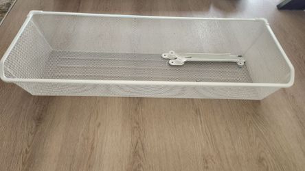 IKEA /4 "
White mesh basket drawer with clothes and helmets, part of a wardrobe.
White mesh basket holding folded beige clothes in white storage syste