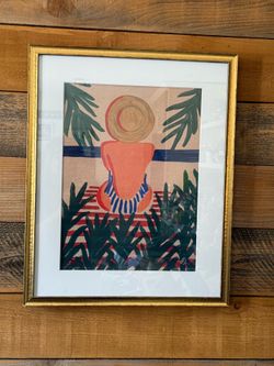 Framed & Matted Vibrant art print by Fabian Lavater depicts a woman in a sun hat and striped swimwear seated among tropical foliage. - Apprx 21” x 17”
