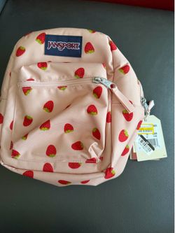 New JanSport mini backpack is pink with a red strawberry pattern. This bag is made of a durable canvas material and has a front zippered pocket and a 
